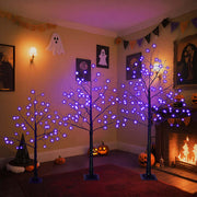 Halloween ghost trees with lights in a spooky decorated room with glowing purple lights and Halloween decor.